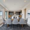 Modern dining room and kitchen interior featuring installed Los Angeles 3-Step Crown Molding along the ceiling and Cincinnati Art Deco Baseboard along the walls, with recessed lighting, gray upholstered chairs, a wood dining table, and dark kitchen cabinetry.
